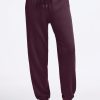 A person is wearing Woolx's Parker Sweatpants in Wine Tasting color with white sneakers, standing against a plain white background. These sweatpants provide travel comfort with features like a drawstring waist, elastic cuffs, and moisture-wicking properties to keep you cozy on the go. | Keesha is 5’9.5”, wearing a size S