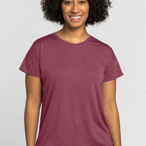 A person with curly hair smiles wearing the Billie Lounge Tee in Wild Ginger by Woolx, recognized for its temperature regulation. The background is plain and light-colored. | Tori is 5'7", wearing a size S