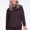 A person with long gray hair is smiling, wearing a dark, long-sleeved Bailey Crewneck Sweatshirt in Chocolate Plum from Woolx. They stand against a neutral background, hands relaxed by their sides. | Tam is 5’8.5”, wearing a size S