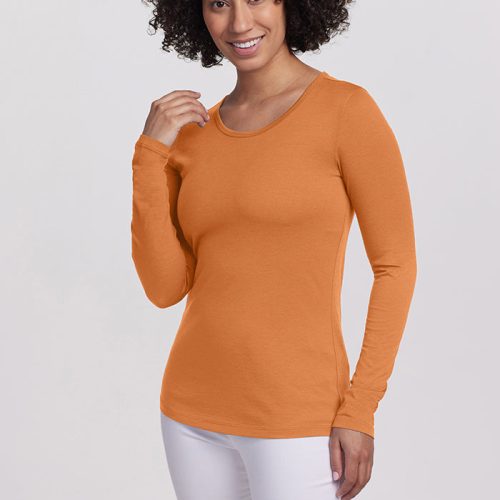 A person with curly hair is smiling, wearing an orange Woolx Remi Long Sleeve TShirt from the Stocking Stuffer Final Sale Deals, paired with white pants. They stand against a plain light gray background, with one hand gently touching their collar.