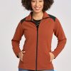 A person with curly hair is smiling, wearing the Woolx Peri Full Zip Jac in Copper, featuring Merino wool and colorblock shoulders, paired with blue jeans. With hands tucked in the jacket pockets, they stand against a plain background.