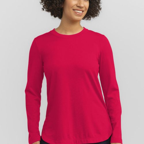 With a smile, a person with curly hair dons the Woolx Hazel Tunic in Viva Magenta, made from lightweight fabric, paired with dark pants. Against a plain white background, they exude effortless style.