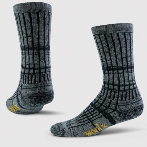 The Joey Full Cushion Mid Calf Socks from Woolx, featuring a dark navy marled color with odor-resistant Merino wool, showcase a black grid pattern and yellow "woolx" branding on the sole. These moisture-wicking socks have a ribbed texture and reach mid-calf length, presented seamlessly against a plain white background.