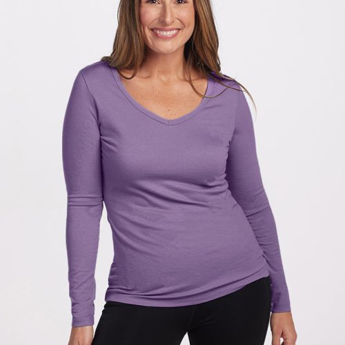 A person with long brown hair smiles while wearing the Woolx Layla V Neck Top in Montana Grape and black pants. They are standing against a plain white background, exuding natural protection and comfort.