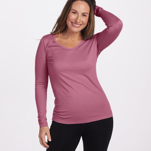 A woman in a Mesa Rose Layla V Neck Top and black leggings is smiling with one hand resting on her head. She stands against a plain white background, embodying the effortless charm of Woolx's Australian Merino Wool.