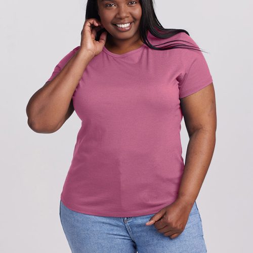 A woman with long dark hair is confidently smiling in a Mesa Rose Liza Crew Neck by Woolx, paired with light blue jeans. She gently touches her hair against a plain gray background that highlights her vibrant style.