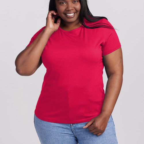 A person wearing a Viva Magenta Liza Crew Neck by Woolx and light blue jeans smiles while standing against a neutral background. Their lightweight top complements their long dark hair as they touch their neck with one hand.