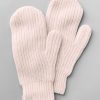 A pair of cozy Holly Mittens in an almost mauve shade lies on a light gray background. Made by Woolx using temperature-regulating Merino wool, these mittens have a distinctive ribbed texture and feature a small tag with a whimsical design attached to the cuff of one mitten.