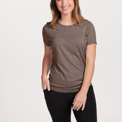 A person with long brown hair is smiling, wearing a lightweight Simply Taupe Liza Crew Neck by Woolx and black pants, standing against a plain white background.