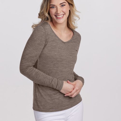 A person with long hair is smiling, wearing the Woolx Layla V Neck Top and white pants. They are standing against a plain white background.