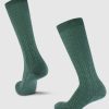 A pair of Woolx "Tilly Over The Calf Cable Knit Sock" in Duck Green is displayed, featuring a knee-high Merino wool design with a subtle cable knit pattern. One sock stands upright while the other leans to the side against a plain white background, highlighting their moisture-wicking properties.