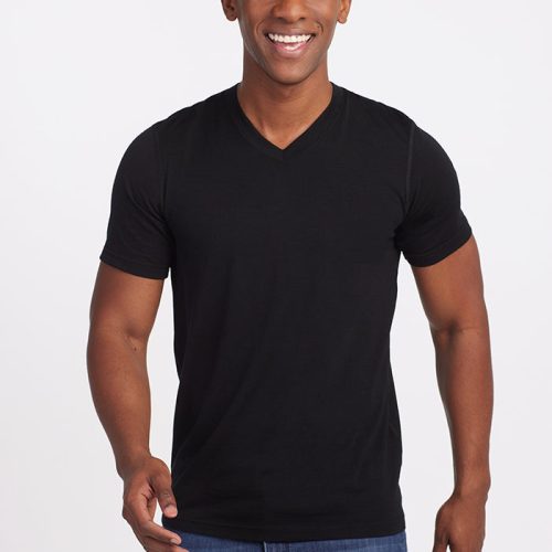 A person smiling, wearing the Ashton V Neck in black by Woolx and blue jeans made from odor-free Woolx DuraLite® Fabric, stands in front of a plain white background.