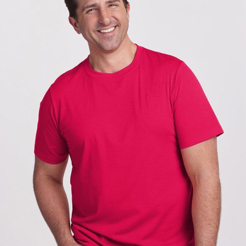 A smiling man wearing a Viva Magenta Endurance Tee by Woolx and dark jeans stands against a plain white background, showcasing his love for performance gear.