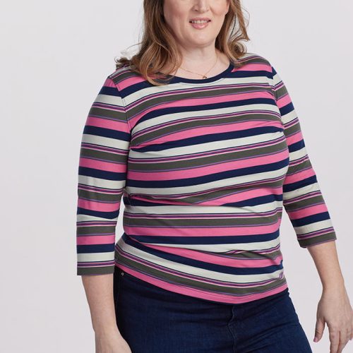 A person with shoulder-length hair is wearing the Woolx Jenny 3/4 Sleeve Crew Neck in Aurora Stripe. Paired with blue jeans, they stand against a plain white background, looking at the camera with a smile.