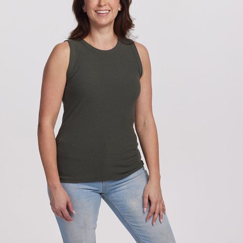 A woman with long brown hair is smiling as she wears the Woolx Raegan Ribbed Tank Top in Deep Fern, paired with light blue jeans, and stands against a plain white background.