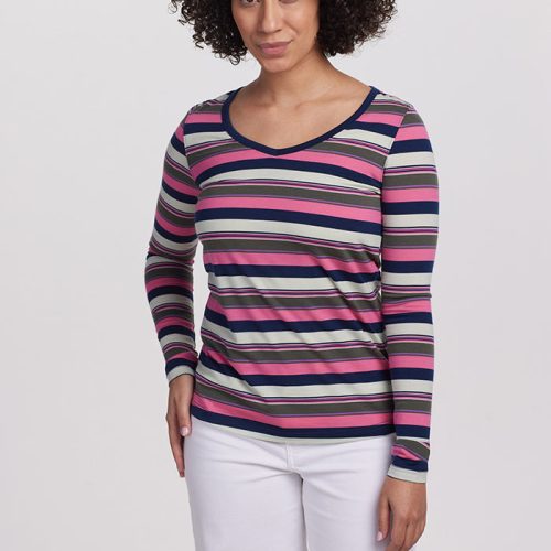 A person wearing the Woolx Layla V Neck Top in Aurora Stripe, displaying purple, pink, black, and white tones. Paired with white pants, they stand against a plain white background, looking at the camera with an air of natural protection.