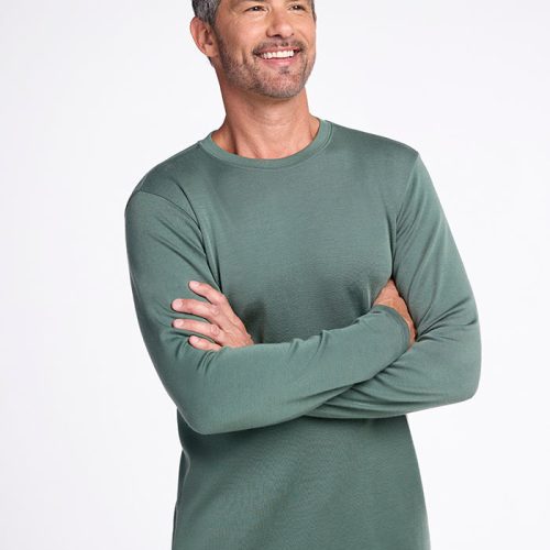 A man with short gray hair smiles while standing with arms crossed, wearing the Woolx Easton Crew Neck Shirt in Duck Green and blue jeans, set against a plain white background.