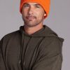 A man with a short beard and mustache is wearing a bright orange Woolx Baylor Beanie and an olive-green hoodie. He is looking directly at the camera with a slight smile. The background is a plain, neutral gray.