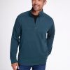 A man with gray hair and a beard smiles while wearing the Woolx Mason 1/4 Zip in Enchanted Forest, crafted from odor-resistant Merino wool fleece, paired with jeans. He stands against a plain white background with his hands relaxed by his sides.