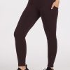 A person wearing the Piper Pocket Petite leggings in French Roast by Woolx, known for their dark brown moisture-wicking material and convenient side pockets, along with black sneakers, stands on a light background. These leggings are specially designed for petite frames.