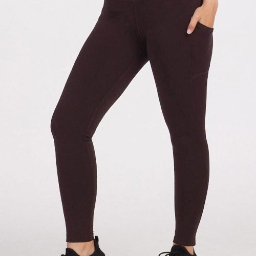 A person wearing Woolx's Piper Pocket Leggings in French Roast and black sneakers stands against a plain background. The image highlights the high-waisted design of the leggings from the waist down.