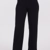 The individual is dressed in the Ellie Wide Leg Pants Petite in black by Woolx, these high-waisted pants feature a chic wide-leg silhouette. They pair the pants with a dark green long-sleeve top tucked neatly into the waistband, and finishing the look with hands in pockets and stylish black ankle boots. The plain white background accentuates their sophisticated fashion choice.