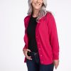 A smiling woman with long gray hair is wearing the Woolx Gia Sweater in Berry Burst over a black top and dark jeans. She stands against a plain white background with her hand in her pocket and the cardigan open. | Tam is 5’8.5”, wearing a size S