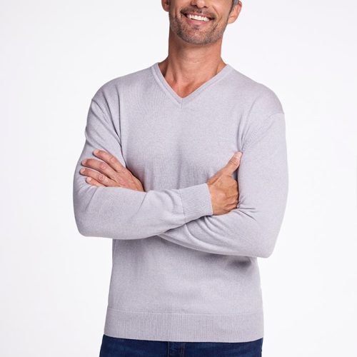 A man with short gray hair and a beard smiles while crossing his arms. He is wearing the Woolx Vincenzo Sweater in Mist paired with blue jeans, standing against a plain white background. | Matthew is 6', wearing a size L