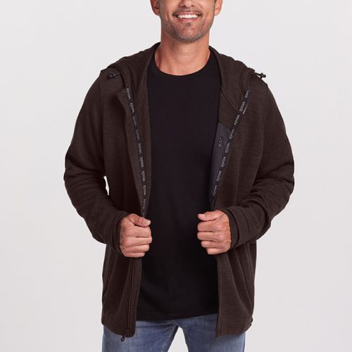 A man with short, greying hair smiles while standing against a plain white background. He is wearing a black t-shirt, jeans, and an unzipped dark brown Woolx Grizzly Sweatshirt in Maple Melange made of ultra-heavyweight Australian Merino Wool. He has his hands lightly holding the sweatshirt edges. | Matthew is 6', wearing a size L