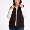 A woman with long brown hair is smiling while wearing the Woolx Colbie Vest in French Roast over a white long-sleeved shirt and blue jeans. She is holding the collar of her vest with both hands, against a plain white background. | Juliana is  5'10", wearing a size XL