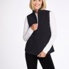 A smiling person with shoulder-length blonde hair is wearing a white long-sleeve shirt under the Woolx Colbie Vest in Carbon Black. They are standing against a plain white background and holding the vest with one hand near the zipper. | Georgia is 5'10", wearing a size XS