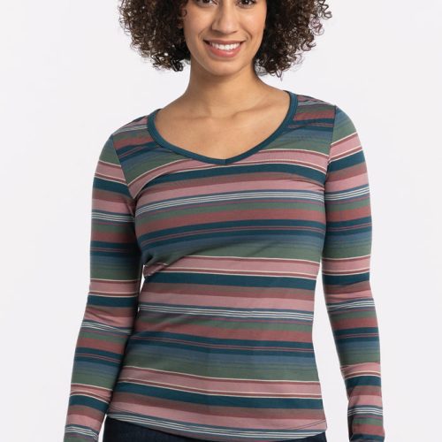 A person with curly hair smiles at the camera, wearing a vibrant Layla V Neck Top - Adirondack 2.0 Stripe from Woolx and dark jeans against a plain background. | Tori is 5'7", wearing a size S