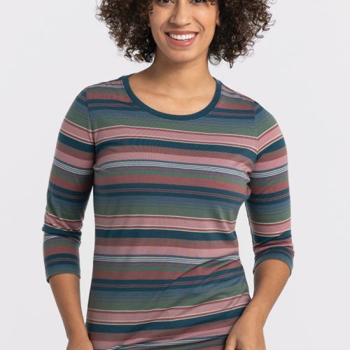 A person with curly hair smiles, wearing the Woolx Jenny 3/4 Sleeve Crew Neck in Adirondack 2.0 Stripe with dark jeans, standing against a plain, light background. | Tori is 5'7", wearing a size S