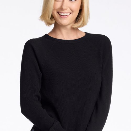 A person with short, blonde hair is smiling while wearing the Woolx Ainsley Sweater in black paired with blue jeans. The background is plain white.  | Georgia is 5'10", wearing a size XS