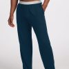 A person wearing Enchanted Forest Arlo Lounge Pants from Woolx, featuring a light gray waistband, stands barefoot against a plain background. One hand is in the pocket of these relaxed-fit travel pants, crafted from odor-free Merino wool for ultimate comfort.