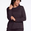 A person wearing the Woolx Ashlie Lounge Top in Chocolate Plum stands against a plain background, smiling and touching their neck with one hand. | Sarah is 5'8", wearing a size S