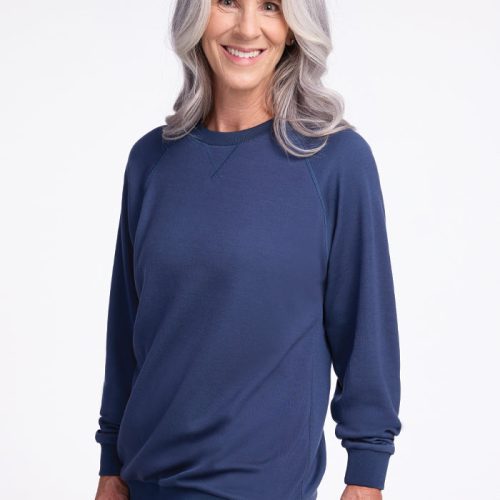 A woman with long gray hair smiles warmly in a Bailey Crewneck Sweatshirt in the Starry Night color from Woolx. She stands against a plain white background, radiating grace and style. | Tam is 5’8.5”, wearing a size S