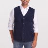 A smiling man with short hair wears a white shirt and the Woolx Baker Vest OLD in dark navy, featuring large pockets and providing insulation even when wet. He pairs it with blue jeans against a plain, light-colored background.