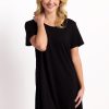 A person with blonde hair smiles while wearing the Desi Nightgown - Black from Woolx, made from Feathertouch® Merino Wool, which is celebrated for its temperature-regulating and odor-resistant qualities. They stand in a relaxed pose against a plain white background. | Kate is 5'7", wearing a size XS