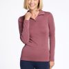 A woman with shoulder-length blonde hair is smiling and posing in a Woolx Brooke 1/4 Zip top in Wild Ginger and dark blue leggings. Her left hand is raised near her chin, against a plain white background. | Georgia is 5'10", wearing a size XS