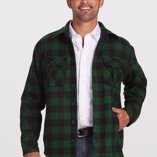 A man wearing a Woolx Burlington Jacket in a green and black plaid pattern over a white shirt and blue jeans stands against a plain background, smiling. His hand is tucked into his jacket pocket, capturing the essence of winter warmth.