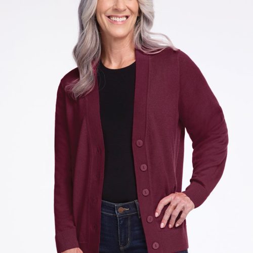 A smiling woman with long gray hair wears the Gia Sweater in Cabernet Crush by Woolx over a black shirt and blue jeans. She stands against a plain white background, with one hand on her hip. | Tam is 5’8.5”, wearing a size S