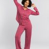 A person in a relaxed pose wears the Harper FeatherTouch® Pajama Set in red violet. Barefoot, they stand against a plain light gray background, smiling with arms playfully raised. The temperature-regulating fabric from Woolx ensures comfort all night long.