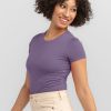 A person with curly hair smiles and looks to the side, showcasing their sunny summer wardrobe. They are wearing the Woolx Gracie Bodysuit, part of the Stocking Stuffer Final Sale Deals, paired with beige pants against a light gray background.