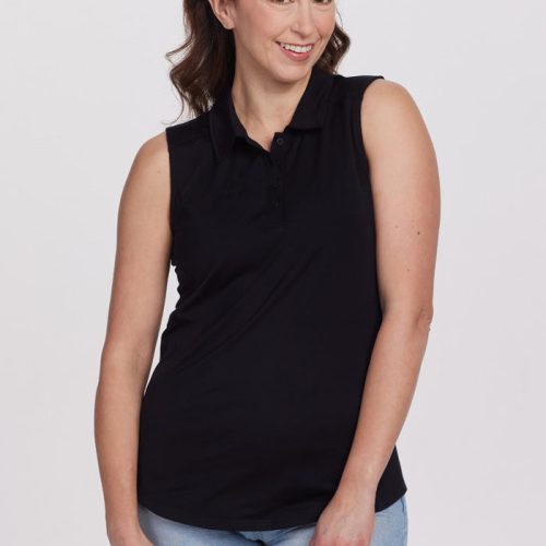 A woman with long brown hair, styled with a beige headband, smiles warmly while standing. She is dressed in a black Rosie Sleeveless Polo from Woolx, crafted from merino wool, and paired with light blue jeans against a plain white background.