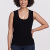 A person with curly hair smiles, wearing a black Woolx Sloane Ribbed Tank OLD and dark jeans that offer a versatile fit. Layered necklaces add a touch of elegance as they stand against a plain background.