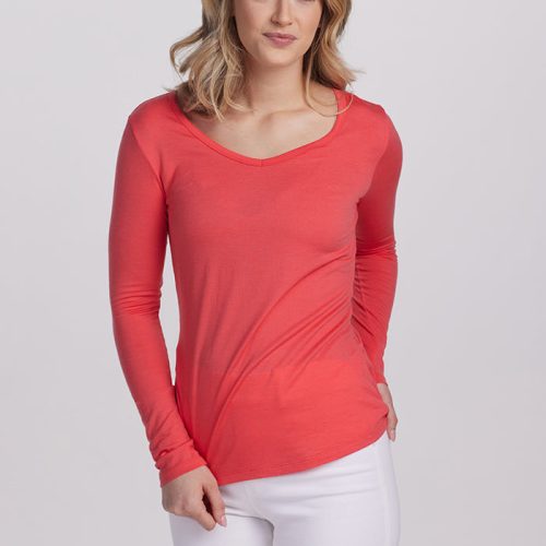 A woman in the Cayenne Layla V Neck Top by Woolx, part of the Stocking Stuffer Final Sale Deals, and white pants stands against a plain background. She has shoulder-length blonde hair and is smiling with her hands by her sides.