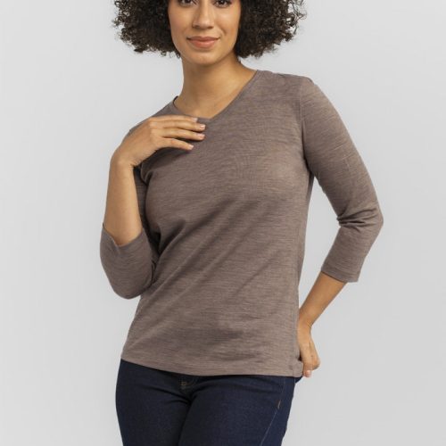 A person with curly hair poses confidently against a plain gray background, wearing a relaxed fit Elena VNeck from Woolx and dark jeans.