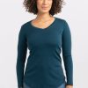 A person with curly hair is wearing a flattering fit, Woolx Eva Tunic in Real Teal, paired with blue jeans, standing against a plain white background.