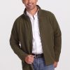 A man wearing a white shirt and an olive green Fairbanks Jacket by Woolx stands smiling with one hand in his jeans pocket, set against a plain gray background. | Matthew is 6', wearing a size L